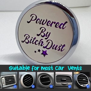 May include: A silver car air freshener with the text "Powered By Bitch Dust" in purple glitter lettering. The air freshener is suitable for most car vents.