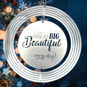 Könnte beinhalten: Ein silberner Windspiel aus Metall mit einem runden Design. Das Windspiel hat ein Zitat, das lautet: "Es gibt einen großen, schönen Morgen, der am Ende jedes Tages strahlt!"