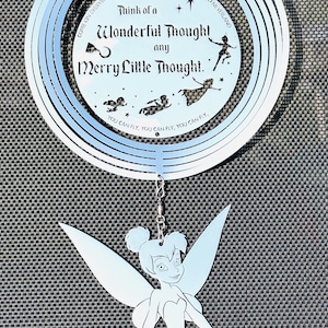 May include: A silver wind chime with a blue tint features a Tinkerbell silhouette and the text "Think of a Wonderful Thought any Merry Little Thought." The chime is suspended from a silver chain.