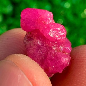 Pode incluir: Um cristal de rubi rosa vibrante com uma textura áspera e natural. O cristal é de uma cor rosa intensa e rica e tem uma forma ligeiramente irregular.