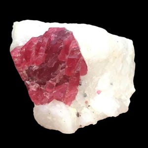 Könnte beinhalten: Ein Cluster aus tief roten Rubin-Kristallen, eingebettet in eine weiße Matrix. Die Kristalle sind scharf und gut definiert, mit einem glasartigen Glanz.