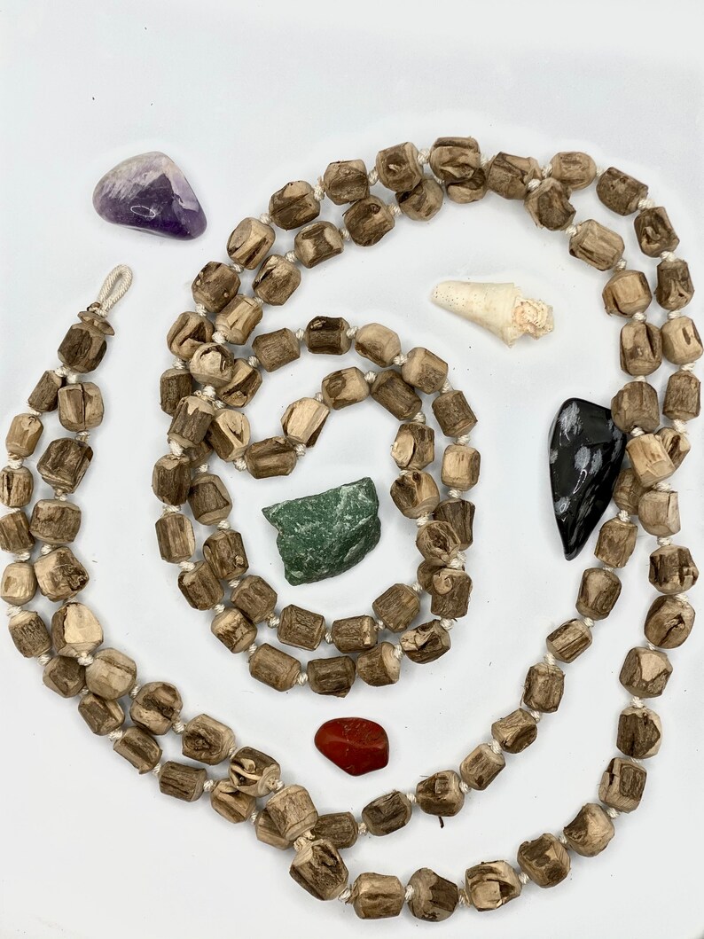 May include: A long strand of wooden beads in a light brown colour with a natural wood grain pattern. The beads are strung together with white string. There are several small stones and crystals scattered around the beads, including a purple amethyst, a green stone, a red stone, a white shell, and a black and white stone.