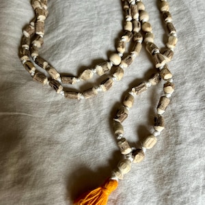 May include: A long strand of wooden beads with a white string threaded through them. The beads are brown and white and have a natural, rustic look. The strand has a small orange tassel at the end.