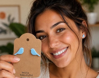 May include: Light blue bird-shaped earrings displayed on a brown tag with the text "hello beautiful". The earrings are also worn by the person in the image. The earrings are a charming accessory.