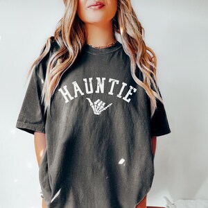 May include: A dark gray oversized t-shirt with the text "HAUNTIE" in white with a skeleton hand graphic.