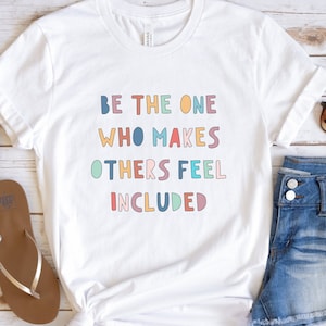 May include: White t-shirt with the text "BE THE ONE WHO MAKES OTHERS FEEL INCLUDED" in colorful letters.