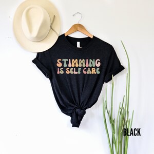May include: Black t-shirt with the text "Stimming is Self Care" in rainbow coloured letters.