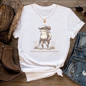 May include: White t-shirt featuring a cartoon image of a frog wearing a cowboy hat and holding a gun. The text "You just yeed your last haw partner" is printed below the image.