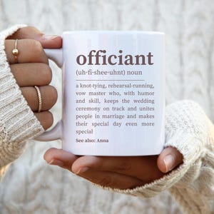 May include: White ceramic mug with the word "officiant" and its definition printed in brown text. The definition reads: "(uh-fi-shee-uhnt) noun a knot-tying, rehearsal-running, vow master who, with humor and skill, keeps the wedding ceremony on track and unites people in marriage and makes their special day even more special. See also: Anna"