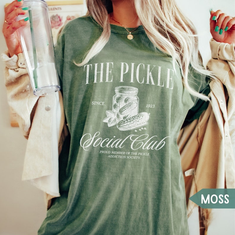 May include: Green t-shirt with a white graphic of a jar of pickles and the text "The Pickle Social Club Since 1923. Proud member of the pickle addiction society."