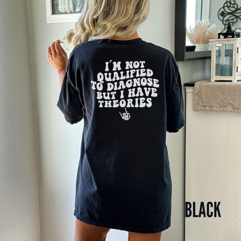 May include: Black oversized t-shirt with the text "I'm not qualified to diagnose but I have theories" in white with a skeleton hand giving the middle finger.
