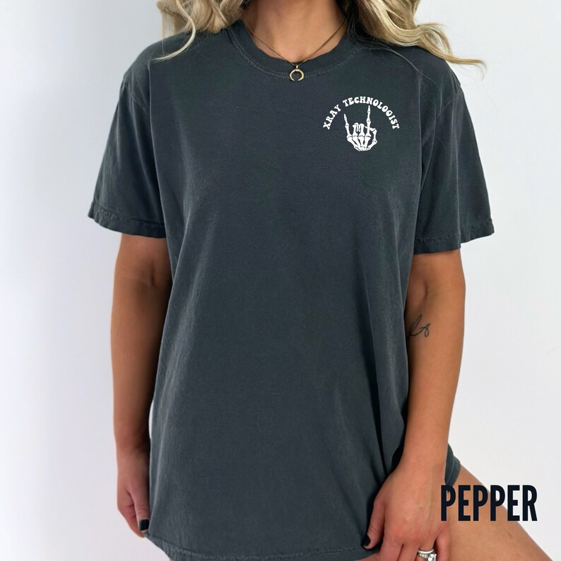 May include: A dark gray t-shirt with a white graphic of a skeleton hand giving the rock and roll sign. The text "X-RAY TECHNOLOGIST" is written in a circle around the hand.