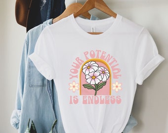 May include: White t-shirt with a pink and yellow graphic design featuring three white flowers and the text "YOUR POTENTIAL IS ENDLESS".