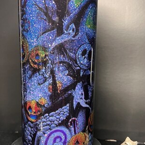 Może przedstawiać: Niebieski i zielony kubek z brokatem z motywem Halloween przedstawiającym Jacka Skellingtona z filmu Koszmar przed świętami. Wz&oacute;r zawiera dynie, laski cukrowe i straszne drzewo.