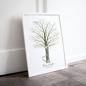 May include: A framed watercolor print featuring a tree with a heart-shaped wreath at the base and two blue birds perched on top. The tree has a banner of white flags. The names "Thomas & Sophie" and the date are printed at the bottom.