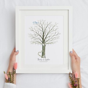 May include: A framed watercolor print featuring a tree with a heart-shaped base and two blue birds. The tree is decorated with a garland of flags. The print includes the names "Thomas & Sophie" and the date.