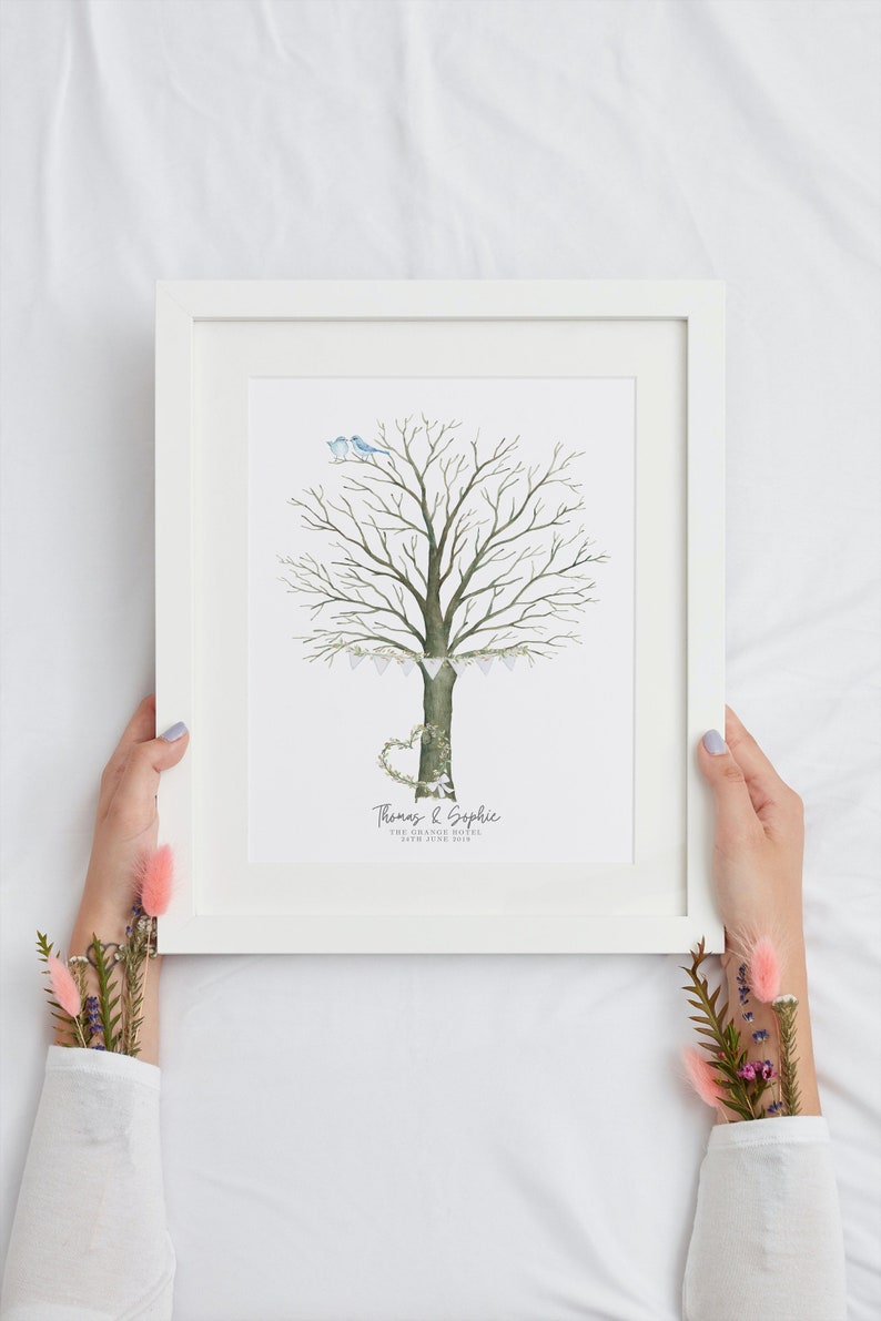 May include: A framed watercolor print featuring a tree with a heart-shaped base and two blue birds. The tree is decorated with a garland of flags. The print includes the names "Thomas & Sophie" and the date.
