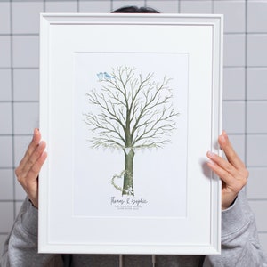 May include: A framed art print featuring a watercolor illustration of a tree with a heart-shaped wreath and two blue birds. The tree has a banner of small white flags. The names "Thomas & Sophie" and the date "24th June 2019" are printed below the tree.