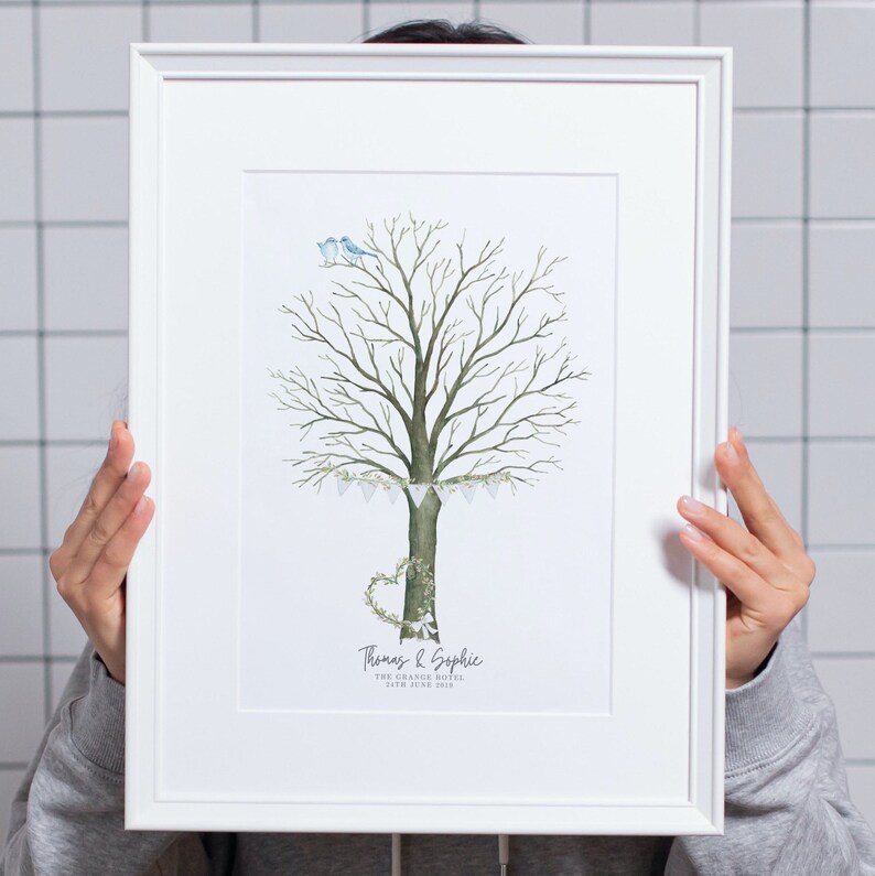 May include: A framed art print featuring a watercolor illustration of a tree with a heart-shaped wreath and two blue birds. The tree has a banner of small white flags. The names "Thomas & Sophie" and the date "24th June 2019" are printed below the tree.