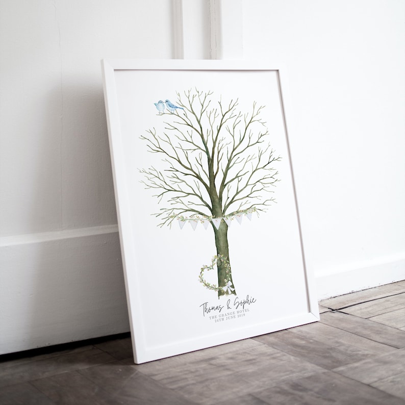 May include: A framed watercolor print featuring a tree with a heart-shaped wreath at the base and two blue birds perched on top. The tree has a banner of white flags. The names "Thomas & Sophie" and the date are printed at the bottom.