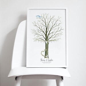 May include: A framed watercolor print featuring a tree with a heart-shaped wreath and a banner of small flags. Two blue birds perch atop the tree. The print includes names and a date, likely for a wedding or special event.
