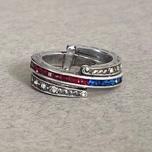 Puede incluir: Anillo plateado con piedras rojas, azules y transparentes. El anillo presenta un diseño en capas con una fila de piedras rojas, una fila de piedras azules y una fila de piedras transparentes.