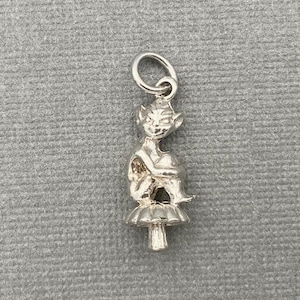 Peut inclure: Charme en argent d'une petite fée assise sur un champignon. La fée a des oreilles pointues et porte une robe. Le champignon a un chapeau blanc et une tige brune.