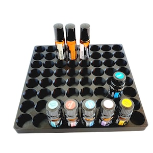 May include: Black essential oil storage tray with 48 round slots. The tray is filled with various essential oil bottles, including bottles labeled "Copaiba", "Motivate", "Magnolia", "Aroma Touch", "Joy", "Peace", and "Terra Shield".