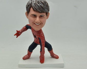 May include: A custom bobblehead figurine of a person dressed as Spider-Man. The figurine is posed with one arm outstretched and the other hand on their hip. The figurine is made of painted ceramic and has a detailed face.