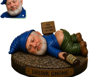 May include: A figurine of a gnome with a white beard wearing a blue hat and shirt, lying on a textured base. The gnome has green pants pulled down, holds a brown bottle labeled Canoe Gnome IPA, and has a sign behind it that reads Too Gnome To Care.