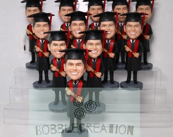 May include: A collection of graduation bobbleheads. Each bobblehead is dressed in a black graduation gown with a red sash and mortarboard. They hold a diploma. The base of each bobblehead reads "Julian Class of 2024".