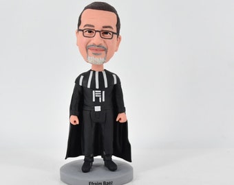 May include: A custom bobblehead figurine of a man wearing a black Darth Vader costume. The figurine is standing on a gray base with the name "Efraim Baez" printed on it.