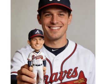 May include: A bobblehead doll of a baseball player wearing a navy blue cap with a white "A" logo and a white and red baseball uniform. The bobblehead is held in front of a person wearing a matching baseball cap and uniform.