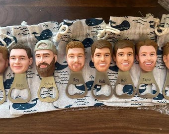 May include: A collection of six metal bottle openers, each featuring a sculpted, hand-painted 3D head of a person with distinct facial features and hair. Each opener is engraved with a name: Isaac, Joshua, Roy, Rob, Rob, and Taylor.