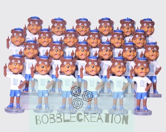 May include: A group of 25 brown bear bobbleheads wearing blue and white shirts with the text "BOLD HEARTS, BRAVE MINDS" and blue hats. The bobbleheads are all standing with their right arms raised and their index fingers pointing up.