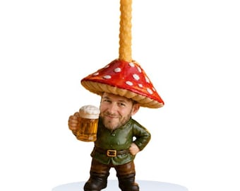 May include: A figurine of a person with a beard wearing a red mushroom cap with white spots as a hat. A tall, textured yellow candle extends from the top of the mushroom. The figure wears a green jacket and holds a glass mug of golden beer.