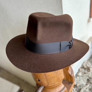 May include: A brown fedora hat with a black ribbon band. The hat is made of felt and has a classic style.