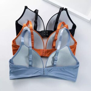 May include: Three bras in different colors: black, orange, and blue. Each bra has adjustable straps and a hook and eye closure in the back. The bras are made of a soft, stretchy fabric.