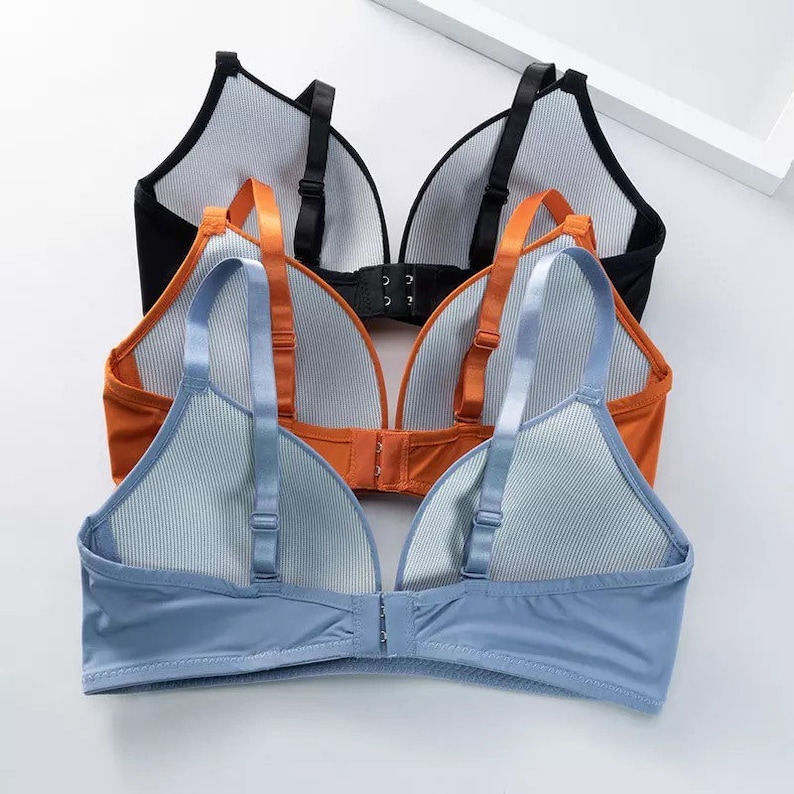 May include: Three bras in different colors: black, orange, and blue. Each bra has adjustable straps and a hook and eye closure in the back. The bras are made of a soft, stretchy fabric.