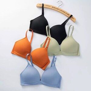 May include: Four different colored bras, black, orange, green, and blue, are stacked on top of each other. The bras are all made of a soft, stretchy material and have adjustable straps.