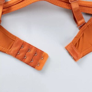 May include: Orange bra strap with a hook and eye closure. The closure has three rows of hooks and eyes.