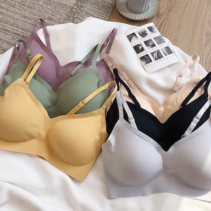 May include: Four seamless bras in different colors: light gray, yellow, green, and purple. The bras have adjustable straps and a V-neckline.