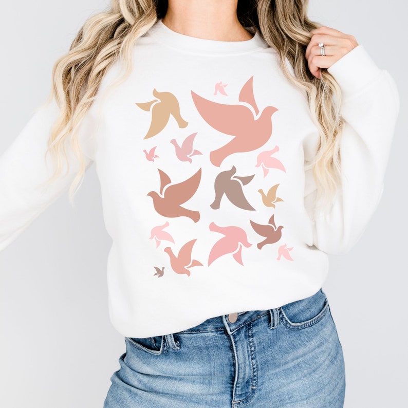 May include: White sweatshirt with a pattern of pink, peach, and brown stylized doves. The doves are all facing the same direction and are arranged in a random pattern.