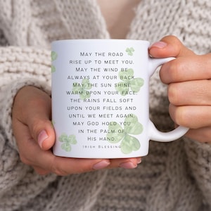 May include: White ceramic mug with a green shamrock design and an Irish blessing printed on it. The text reads: "May the road rise up to meet you. May the wind be always at your back. May the sun shine warm upon your face; the rains fall soft upon your fields and until we meet again. May God hold you in the palm of his hand. Irish Blessing."