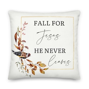 Puede incluir: Una almohada blanca con un marco dorado y un dise&ntilde;o de acuarela de hojas de oto&ntilde;o y un p&aacute;jaro. El texto "Fall for Jesus He Never Leaves" est&aacute; impreso en negro.