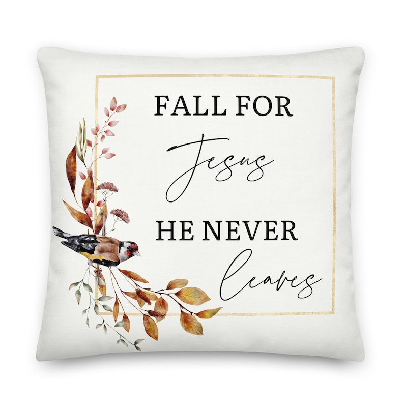 Puede incluir: Una almohada blanca con un marco dorado y un dise&ntilde;o de acuarela de hojas de oto&ntilde;o y un p&aacute;jaro. El texto "Fall for Jesus He Never Leaves" est&aacute; impreso en negro.
