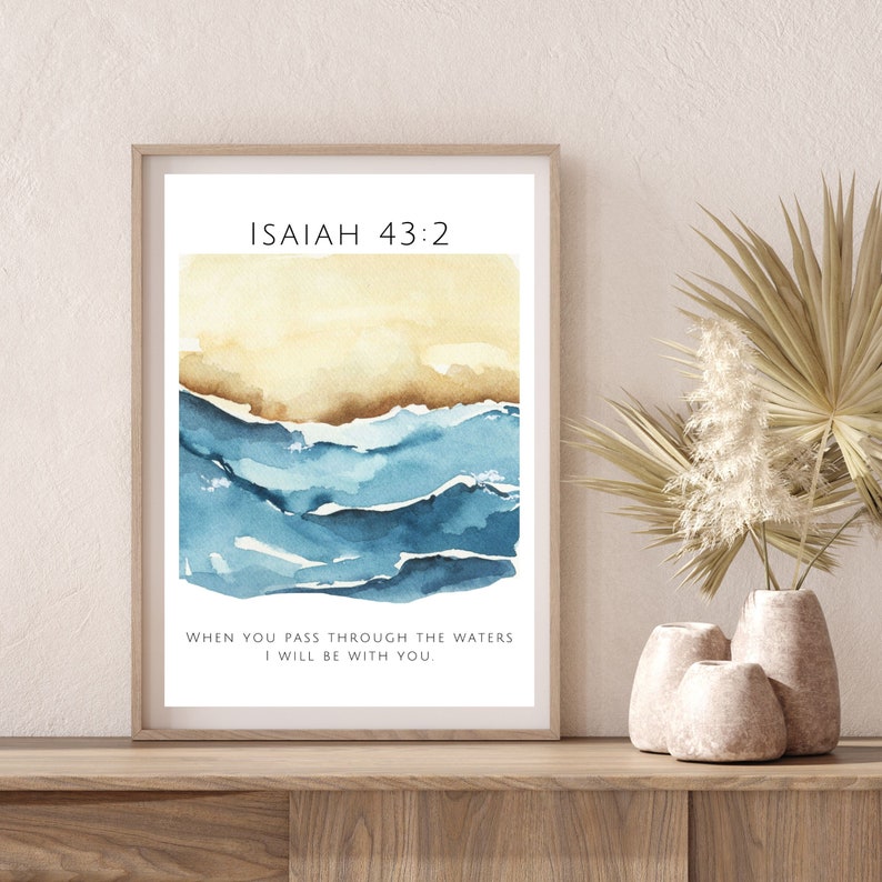Op de afbeelding: Een ingelijst afdruk met een aquarel van blauwe golven en een gele lucht. De afdruk bevat de tekst "ISAIAH 43:2" en "WHEN YOU PASS THROUGH THE WATERS I WILL BE WITH YOU."