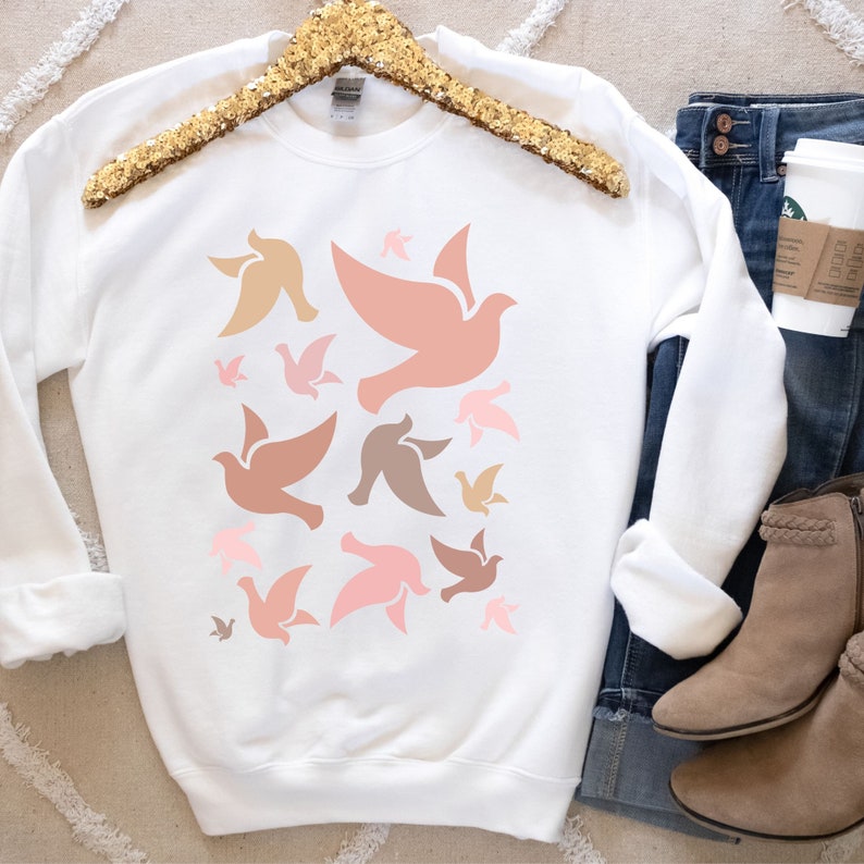 May include: White sweatshirt with a pattern of pink, brown, and beige doves. The doves are all facing the same direction and are arranged in a random pattern.