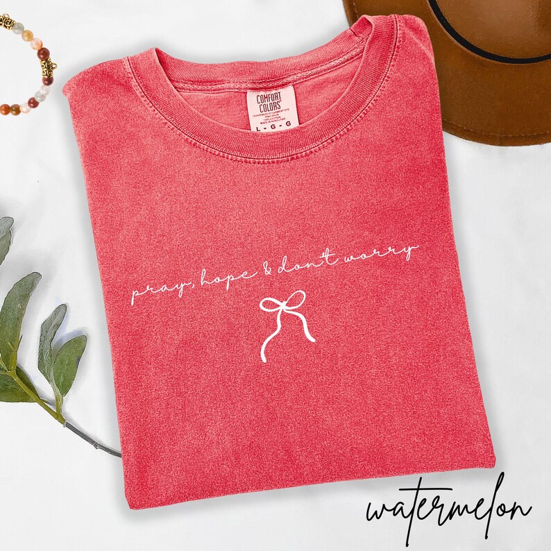 May include: A red t-shirt with the words "pray, hope & don't worry" and a bow graphic in white. The shirt is labeled "Comfort Colors" and the word "watermelon" is written in cursive at the bottom.