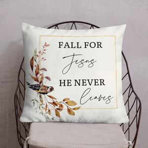 Puede incluir: Una almohada blanca con un marco dorado y un dise&ntilde;o de acuarela de hojas de oto&ntilde;o y un p&aacute;jaro. El texto "Fall for Jesus He Never Leaves" est&aacute; impreso en negro.